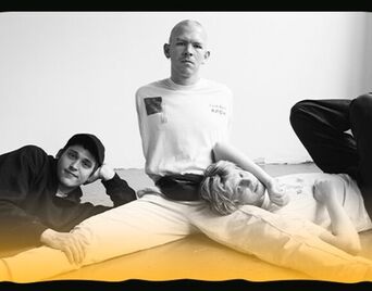 Det sort-hvide foto af tre musikere, der sidder sammen på gulvet i et rum.